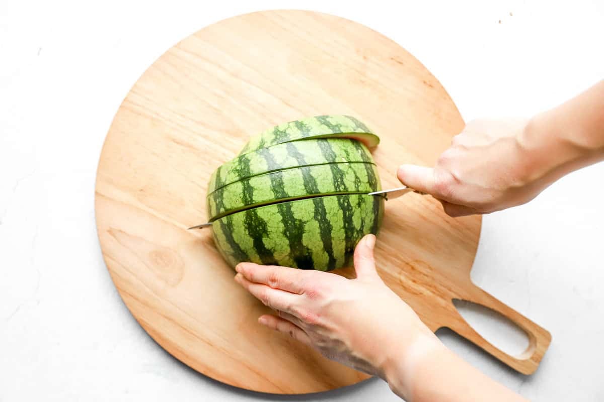 Watermelon being sliced into thick vertical sections with a sharp knife.