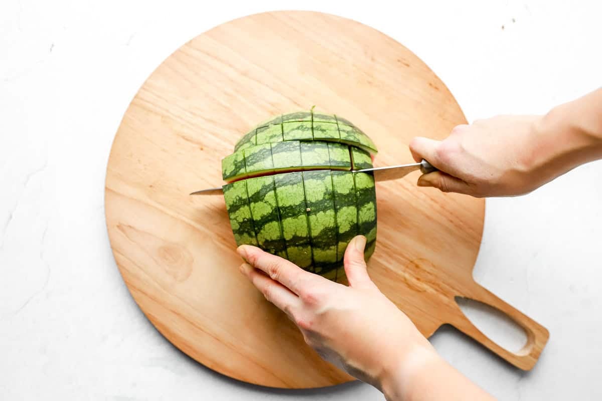 Knife slicing horizontally across a watermelon half to create a grid pattern.