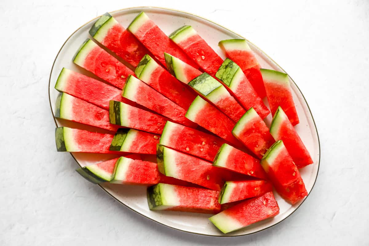 Finished watermelon sticks arranged neatly in a fan shape on a white oval platter, ready to serve.
