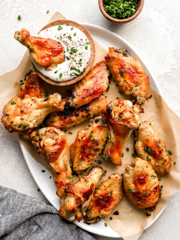 Crispy baked ranch chicken wings on a parchment-lined plate, garnished with fresh chives and served with a bowl of creamy ranch dressing.