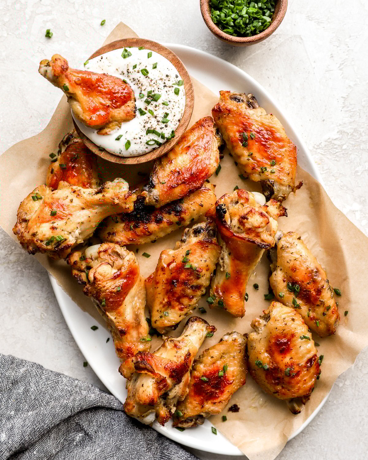 Crispy baked ranch chicken wings on a parchment-lined plate, garnished with fresh chives and served with a bowl of creamy ranch dressing.