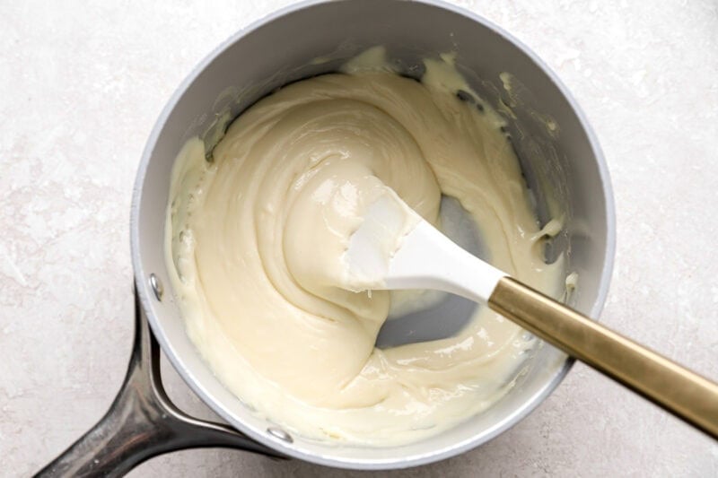 Melted Velveeta cheese being stirred in a saucepan with a white spatula, showing a smooth and creamy texture.