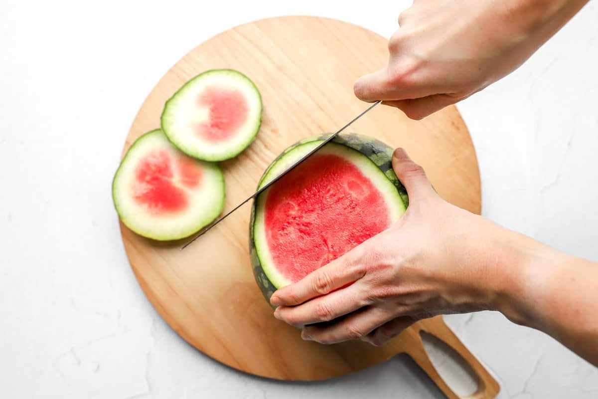 Knife slicing off the bottom end of the watermelon, revealing the red interior.