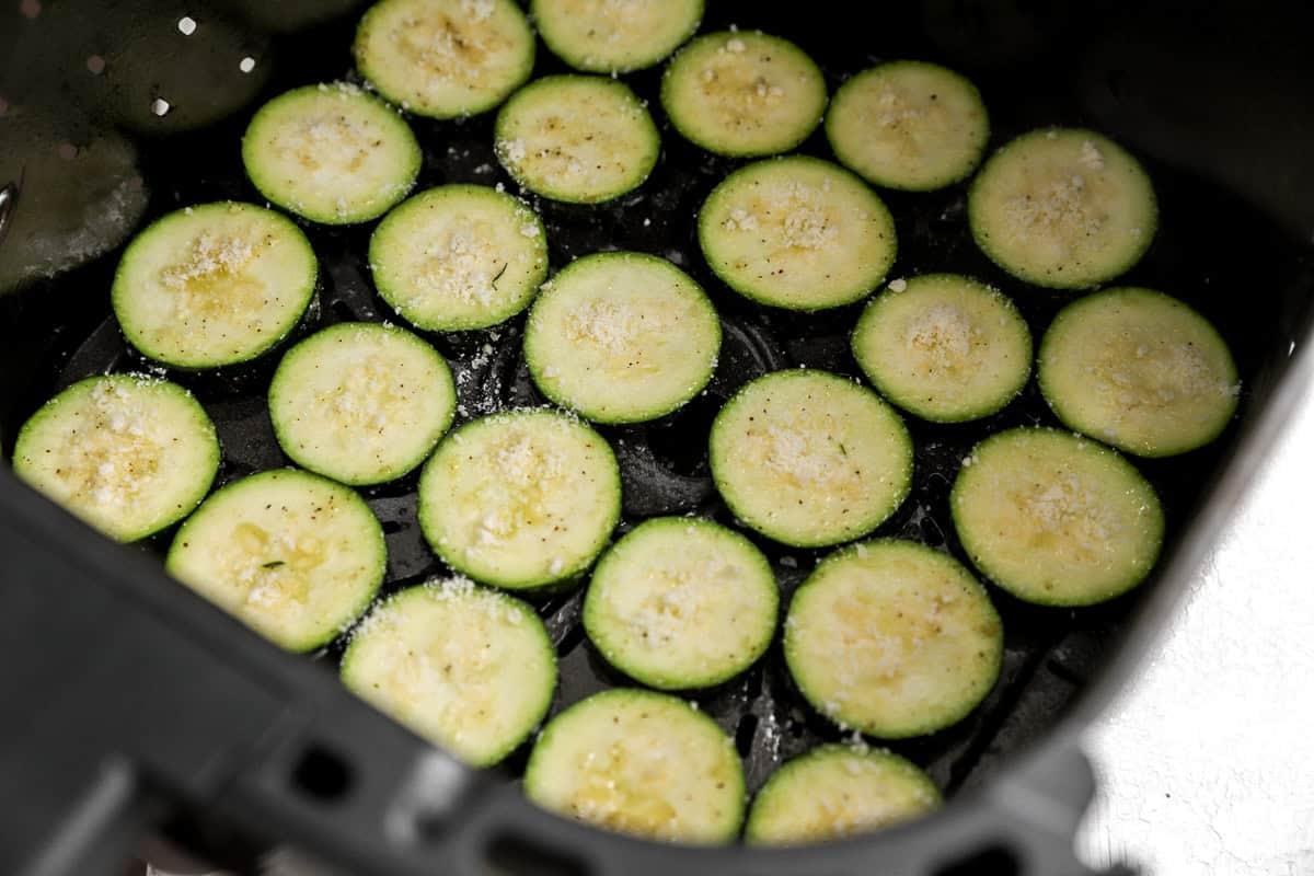 Seasoned zucchini slices arranged in a single layer inside an air fryer basket, topped with a light sprinkle of grated Parmesan.