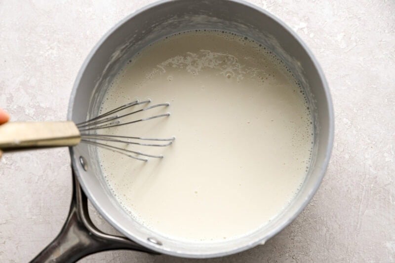 Whole milk and melted Velveeta cheese being stirred in a saucepan with a white spatula, showing a smooth and creamy texture.