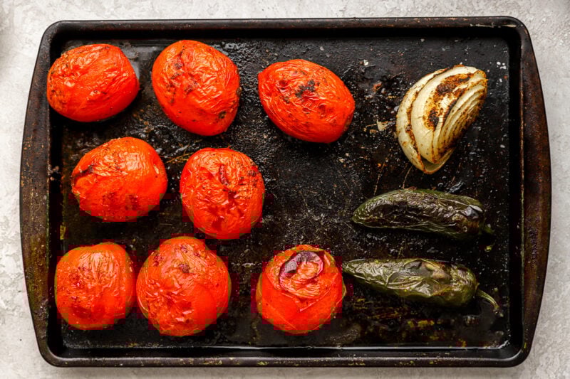 Roasted roma tomatoes, onion, and jalapeños on a baking sheet, with visible char for added flavor.