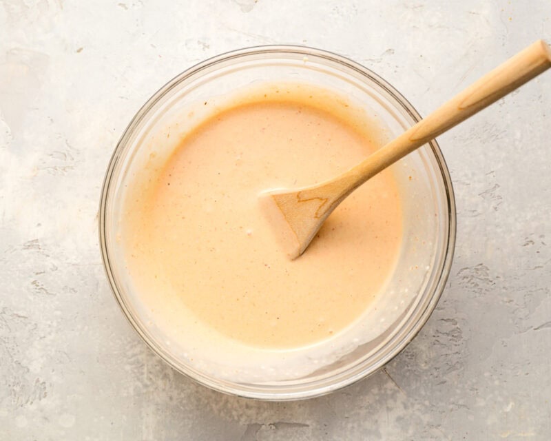 Creamy chipotle mayo sauce in a glass bowl with a wooden spatula, ready for spreading on sandwiches.