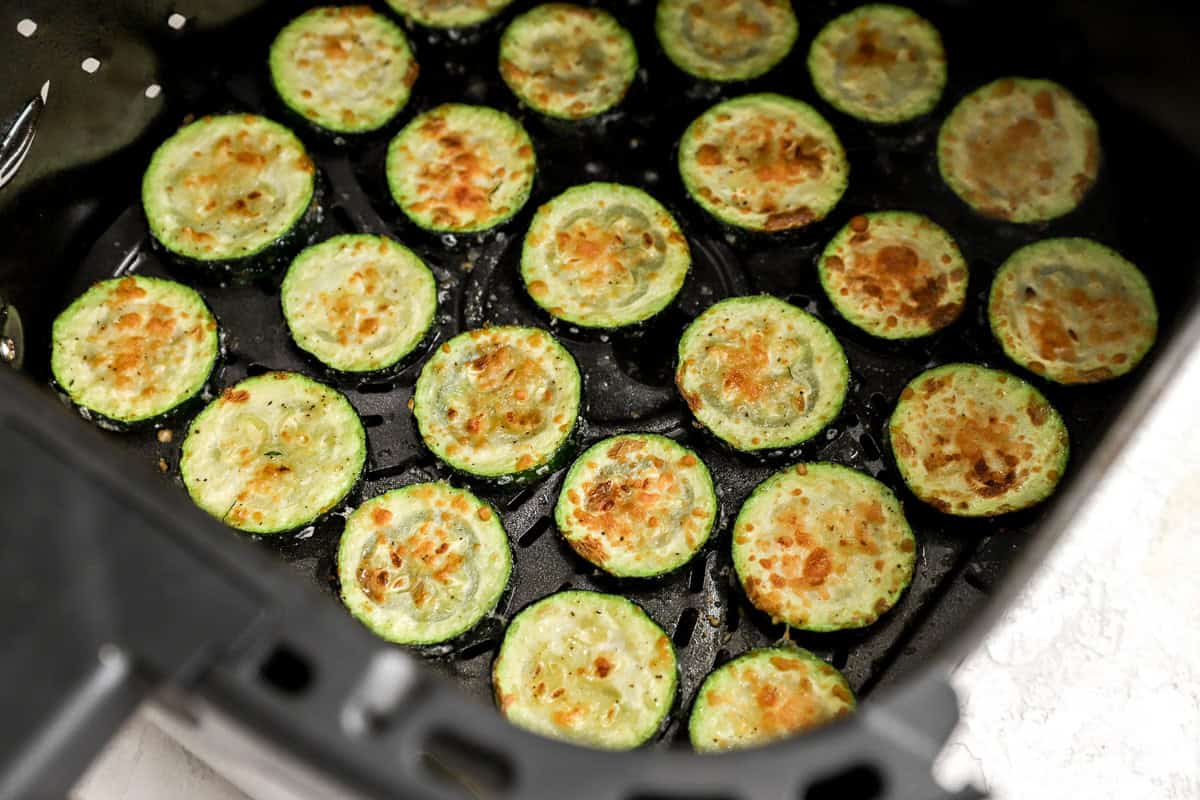 Zucchini slices in the air fryer basket after cooking, with golden, crispy tops and caramelized edges.