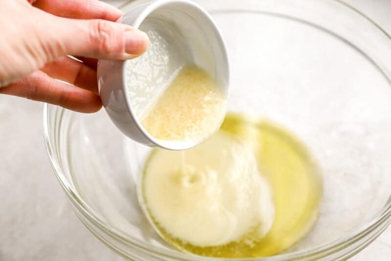 Melted butter being poured from a small white bowl into a bowl of garlic-infused olive oil.