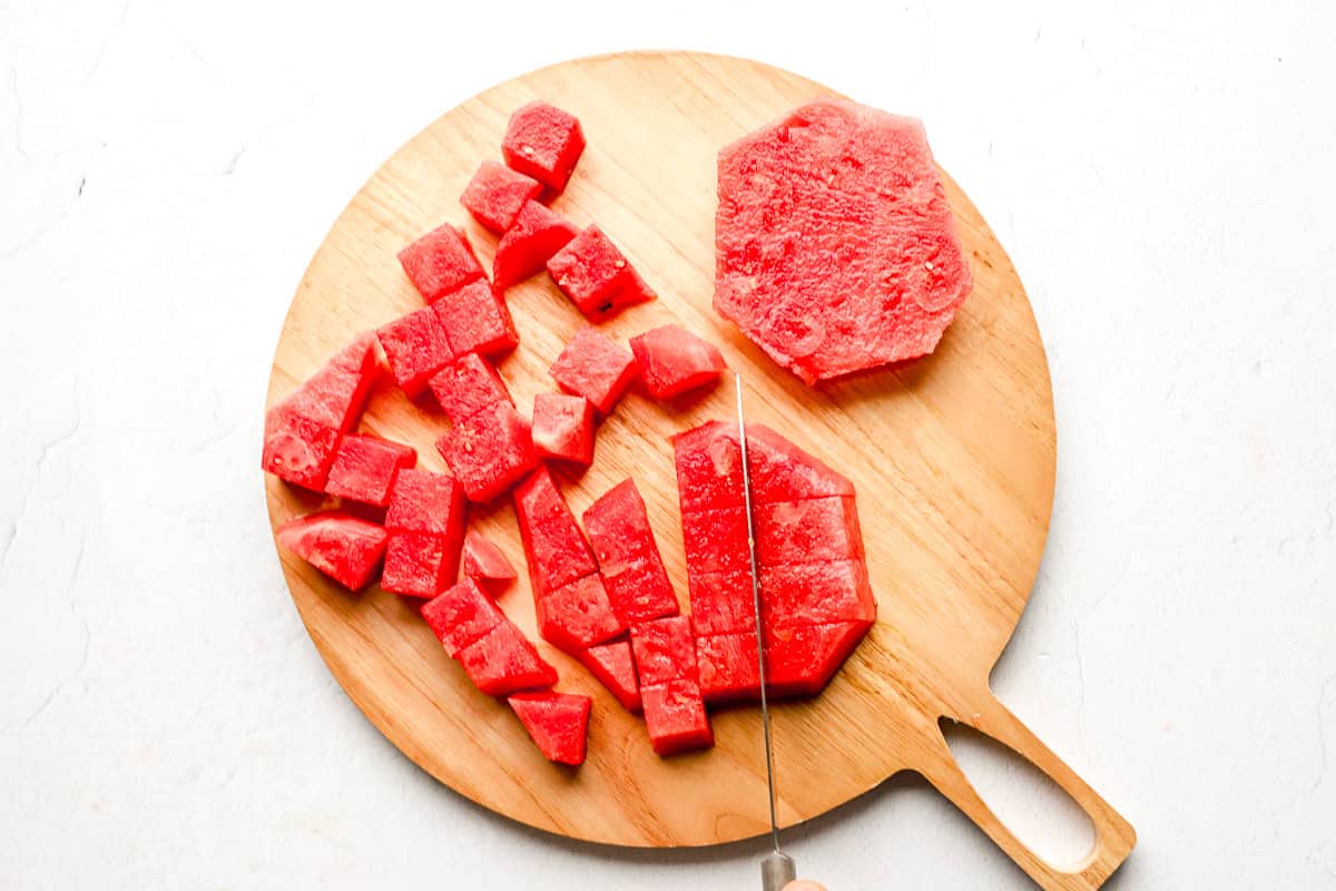 Hands cutting the watermelon rounds into uniform sticks and cubes.