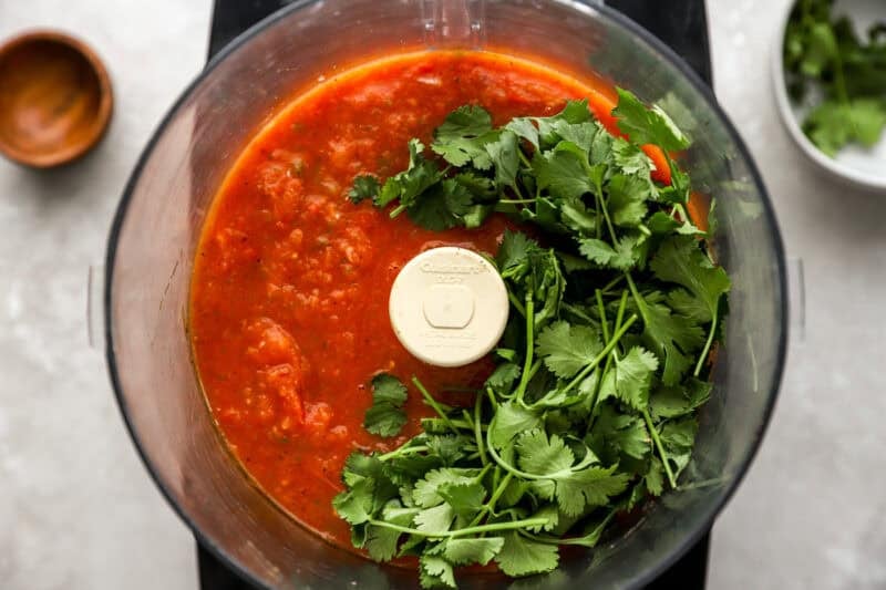 Food processor with blended roasted salsa and a bunch of fresh cilantro added before final blending.