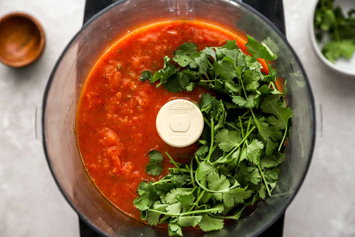 Food processor with blended roasted salsa and a bunch of fresh cilantro added before final blending.