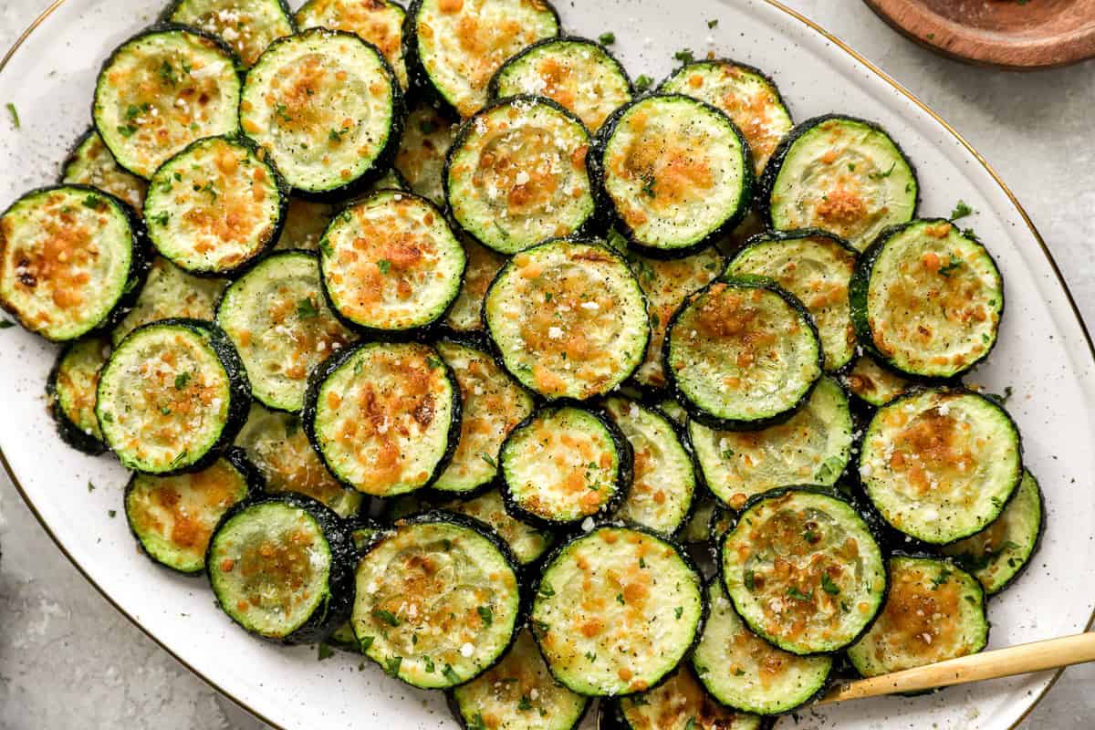 Close-up of air-fried zucchini rounds with golden brown tops, sprinkled with Parmesan and parsley, showing crispy texture.