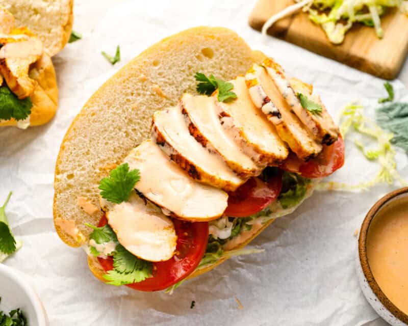 Open-faced chicken torta with sliced grilled chicken, tomato, lettuce, cilantro, and chipotle mayo on a soft bolillo roll.