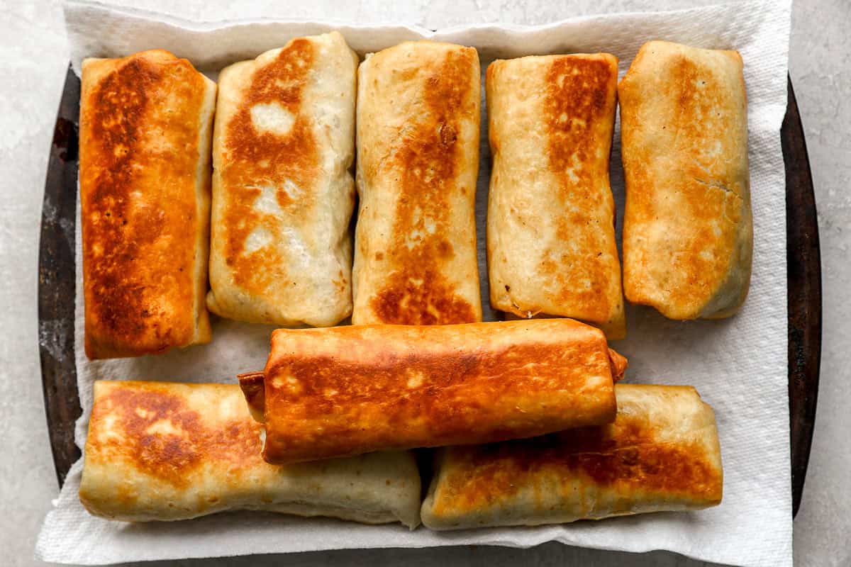 A tray of freshly fried chimichangas resting on a paper towel–lined baking sheet.