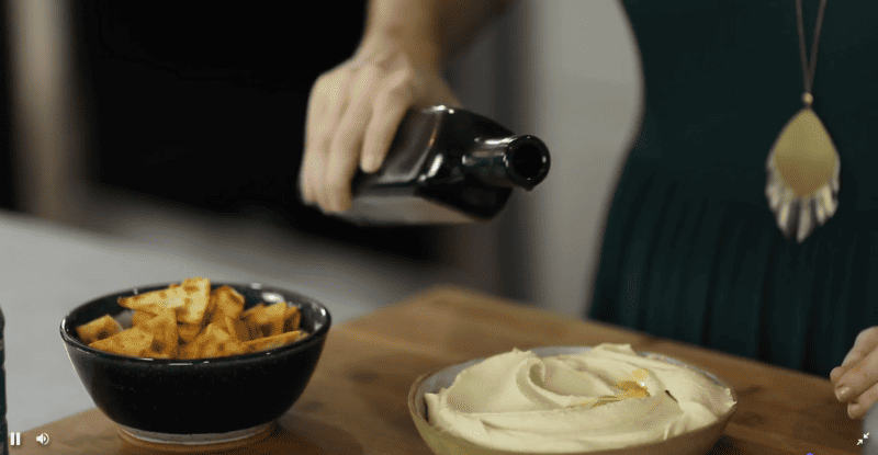 Olive oil being poured over a bowl of hummus.
