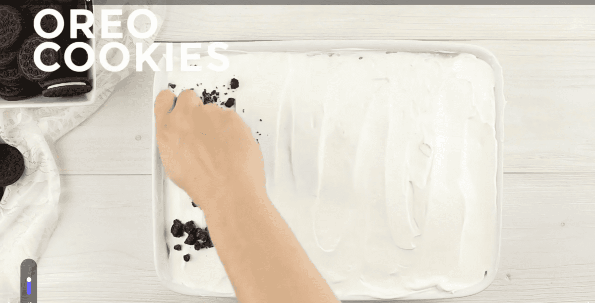 Placing Oreo cooking crumbs on top of poke cake.