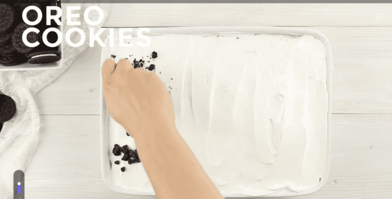 Placing Oreo cooking crumbs on top of poke cake.