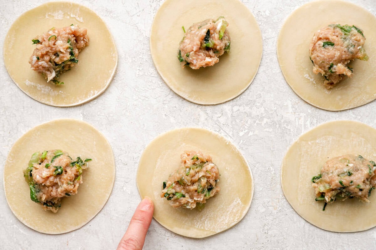 Dumpling wrappers laid out on a surface with a scoop of chicken filling placed in the center of each one.