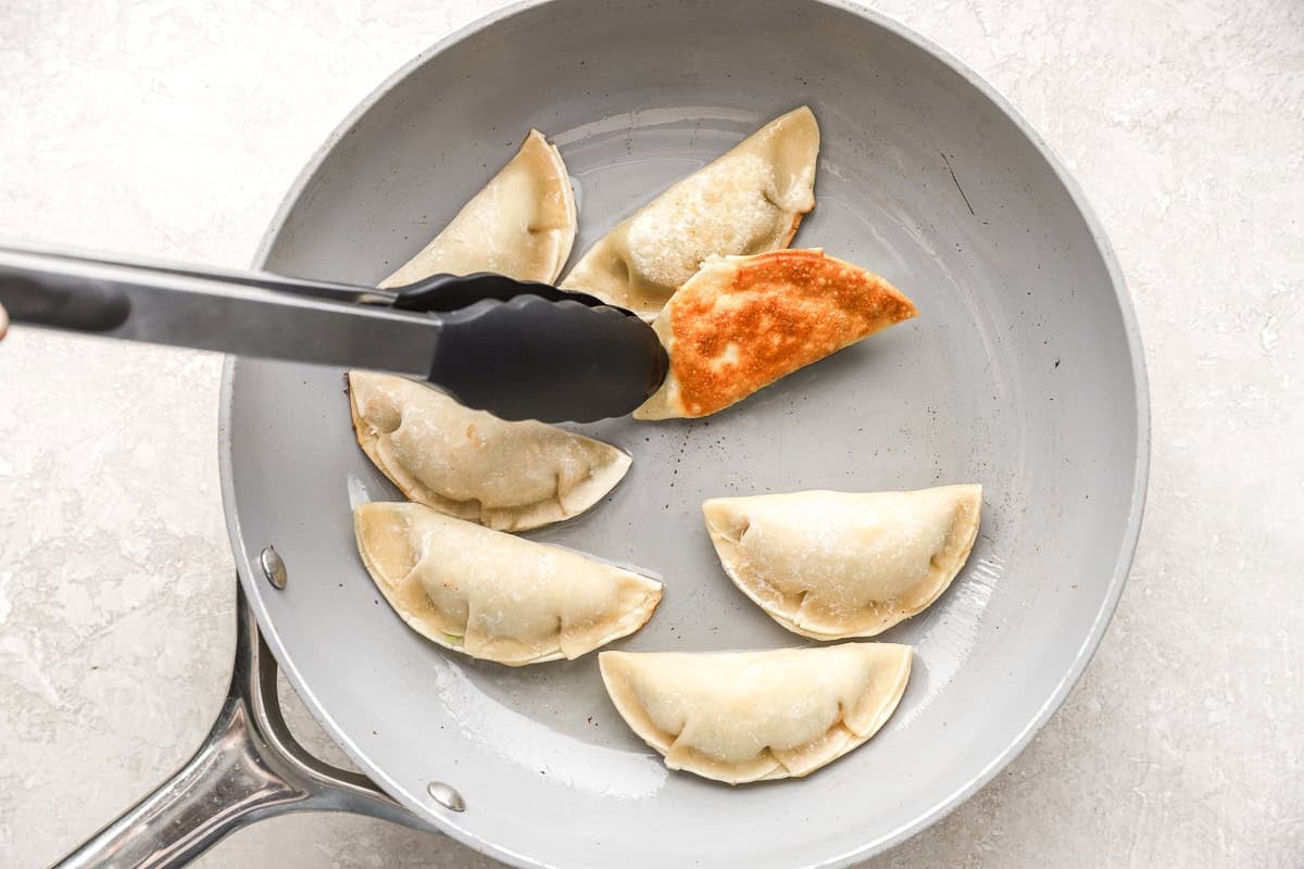 Potstickers cooking in a skillet, with one being flipped to show the crispy golden bottom.