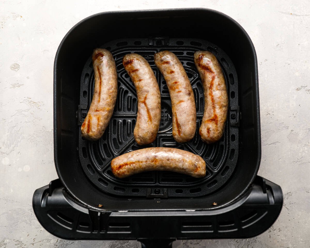 Bratwursts halfway through cooking in the air fryer, starting to brown slightly on the surface.