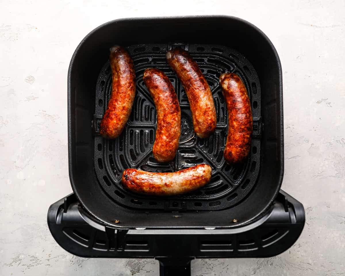 Bratwursts in the air fryer near the end of cooking, fully browned and crisp on the outside.