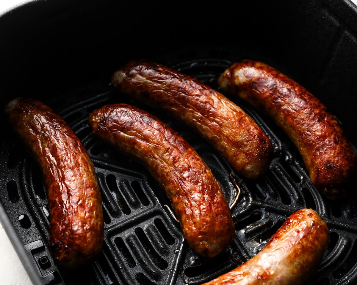 Close-up of finished bratwursts in the air fryer with golden, crispy skin and visible grill lines.