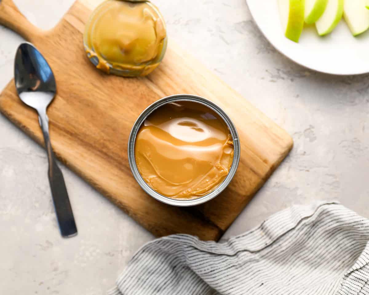 An opened can of caramel on a wooden board, showing the smooth, golden surface of the thickened caramel inside.