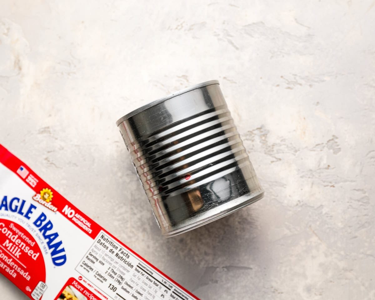 A can of Eagle Brand sweetened condensed milk with the label partially removed, placed on a light surface next to the packaging.
