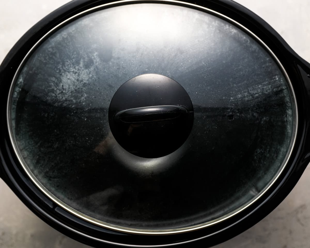 A close-up of a slow cooker with the lid on, steam residue visible on the inside of the glass.