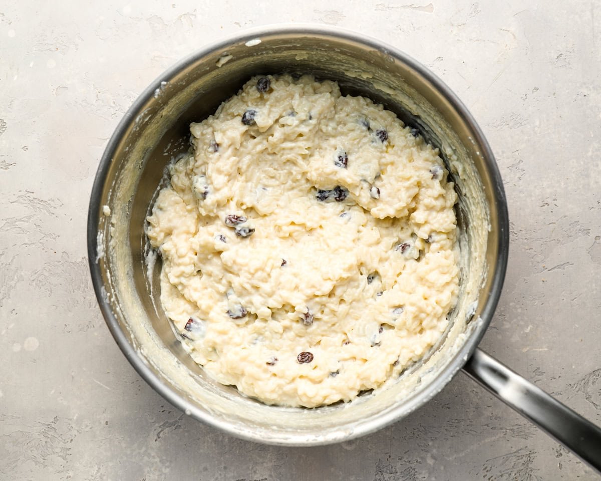 A close-up overhead view of finished rice pudding in a saucepan, showing a thick, creamy consistency with visible raisins.