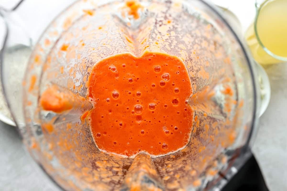 A blender filled with smooth, bright red tomato-pepper mixture used as the base for jollof rice.