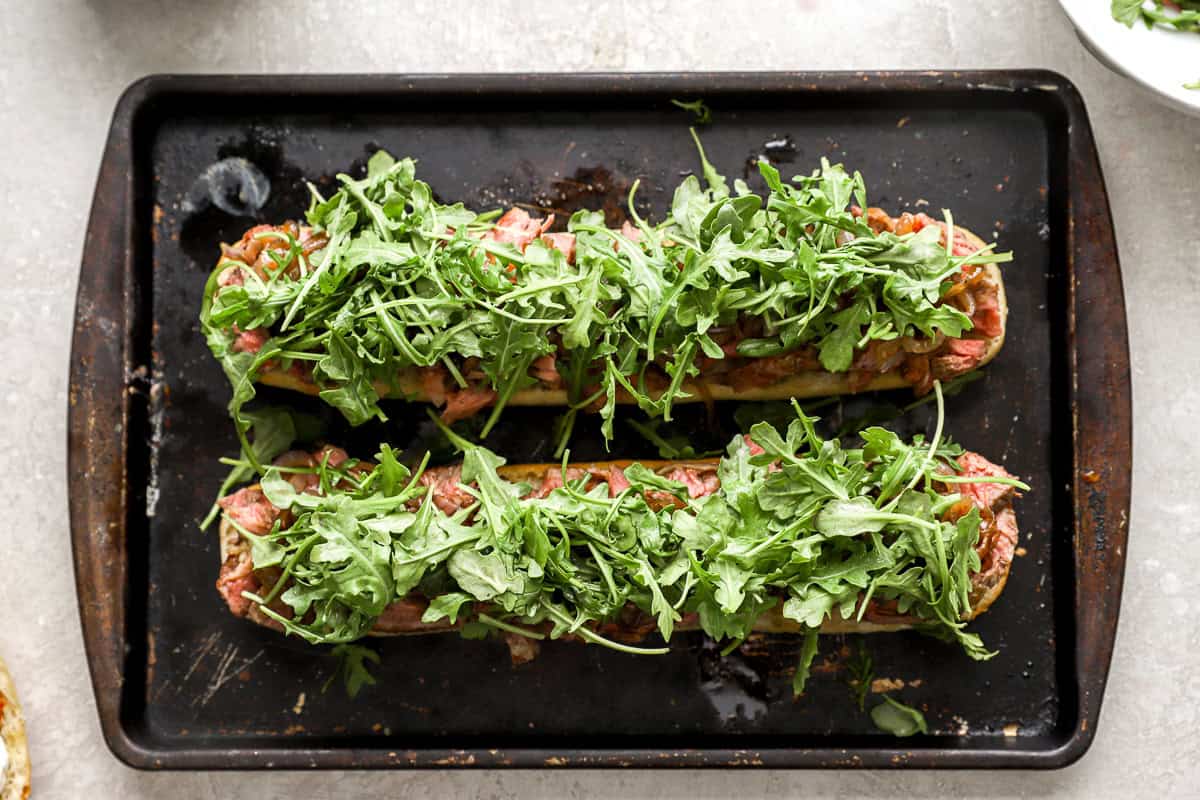 Fresh arugula piled generously over the steak and onion layers on toasted baguette halves.