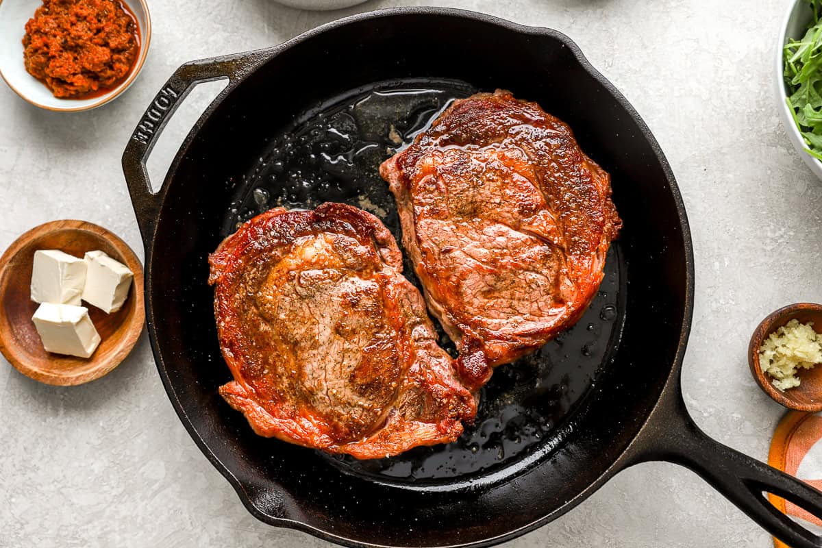 Two perfectly seared ribeye steaks resting in a cast iron skillet with butter melting on top.
