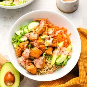 Overhead view of a salmon bowl filled with rice, avocado, shredded carrots, sliced cucumber, green onions, and Bang Bang sauce.