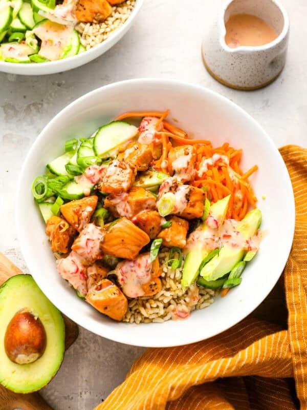 Overhead view of a salmon bowl filled with rice, avocado, shredded carrots, sliced cucumber, green onions, and Bang Bang sauce.