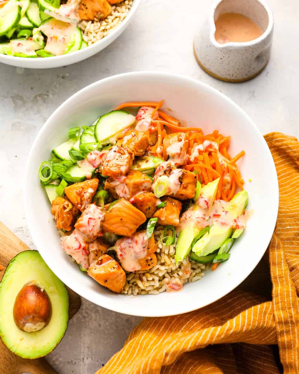 Overhead view of a salmon bowl filled with rice, avocado, shredded carrots, sliced cucumber, green onions, and Bang Bang sauce.

