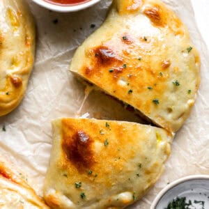 Golden-brown baked calzone sliced in half with melted cheese inside, served with marinara sauce for dipping.