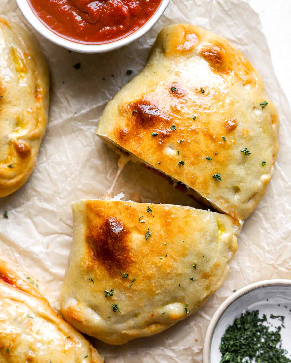 Golden-brown baked calzone sliced in half with melted cheese inside, served with marinara sauce for dipping.