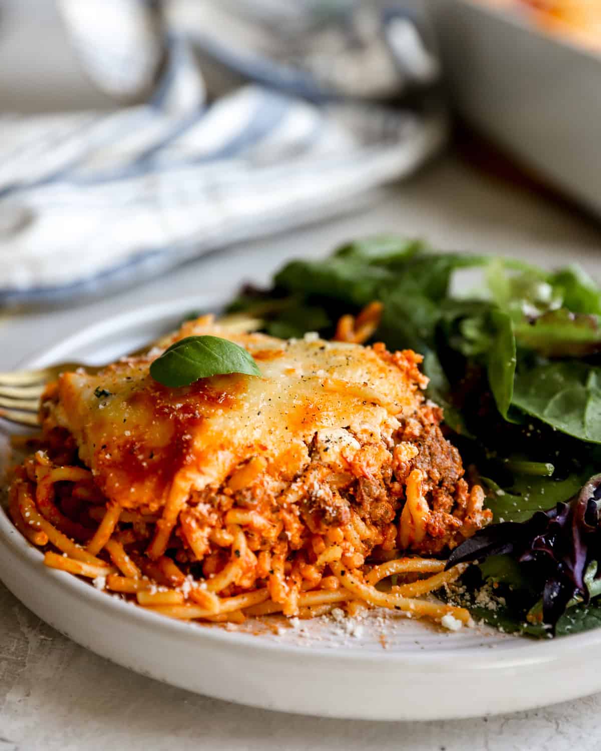 A plated slice of baked million dollar spaghetti topped with melted cheese and fresh basil, served alongside a simple green salad.