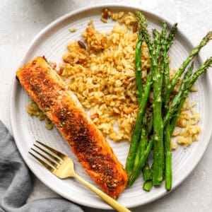 A plate of cooked salmon fillet seasoned with a spice blend, served with golden rice and roasted asparagus.