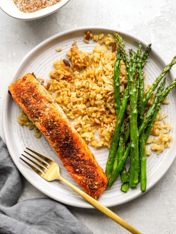 A plate of cooked salmon fillet seasoned with a spice blend, served with golden rice and roasted asparagus.
