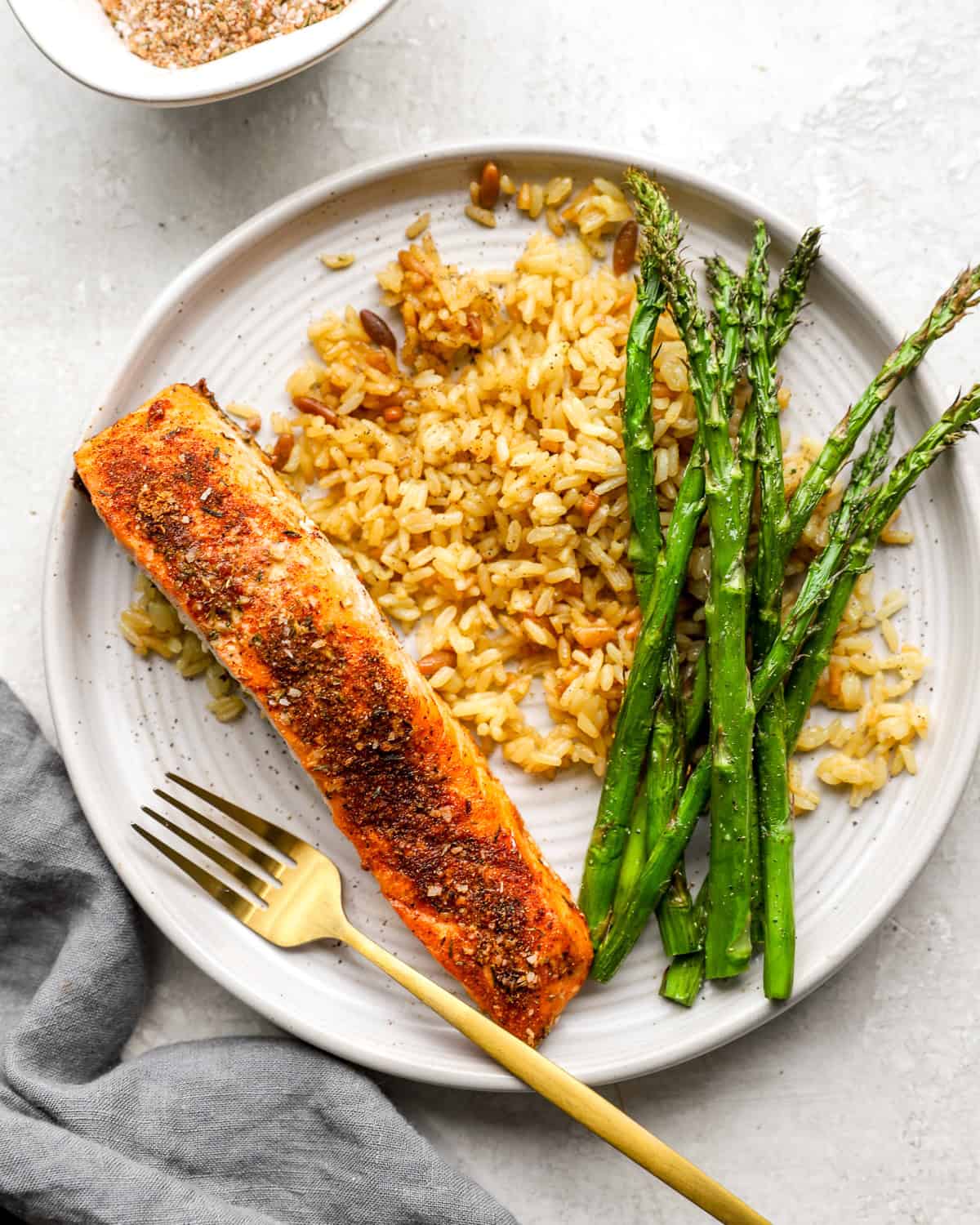 A plate of cooked salmon fillet seasoned with a spice blend, served with golden rice and roasted asparagus.