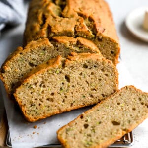 Sliced zucchini bread on a parchment-lined cooling rack, showing a moist, fluffy interior with flecks of shredded zucchini.