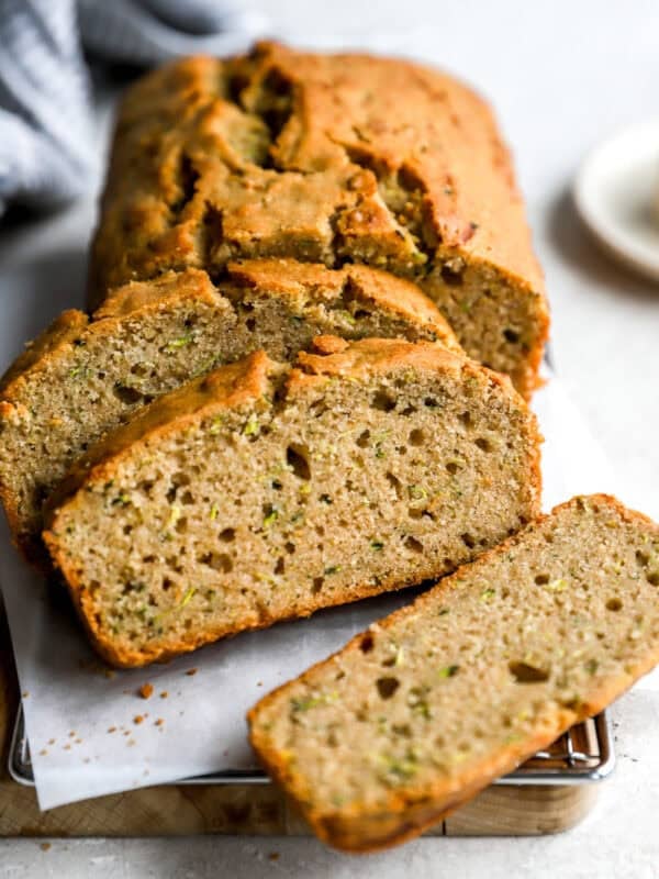 Sliced zucchini bread on a parchment-lined cooling rack, showing a moist, fluffy interior with flecks of shredded zucchini.