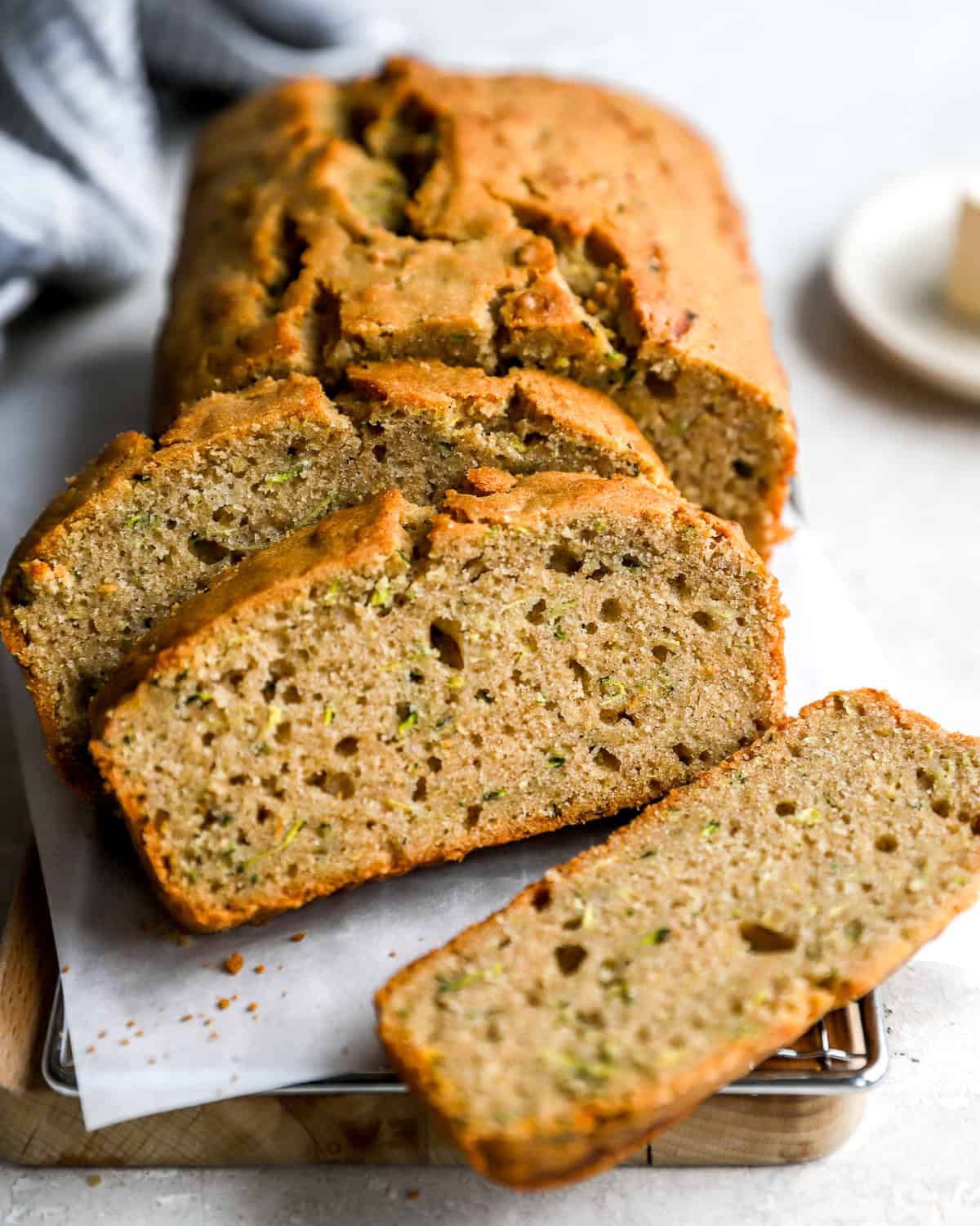 Sliced zucchini bread on a parchment-lined cooling rack, showing a moist, fluffy interior with flecks of shredded zucchini.