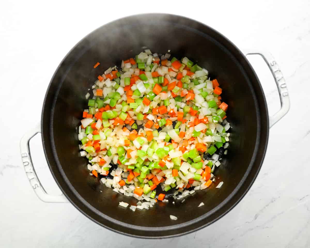 Diced onions, carrots, and celery sautéing in a large black Dutch oven pot.