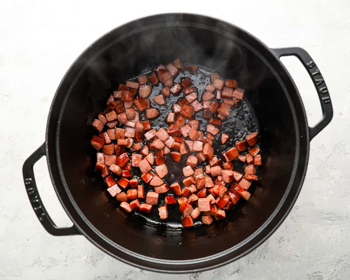 Cubes of smoked sausage sizzling in a pot, starting to brown and crisp on the edges.