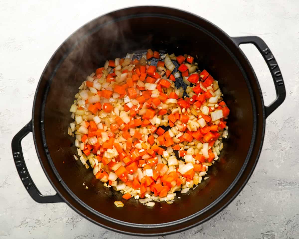 Diced carrots and onions cooking in a black pot, beginning to soften and release their aroma.