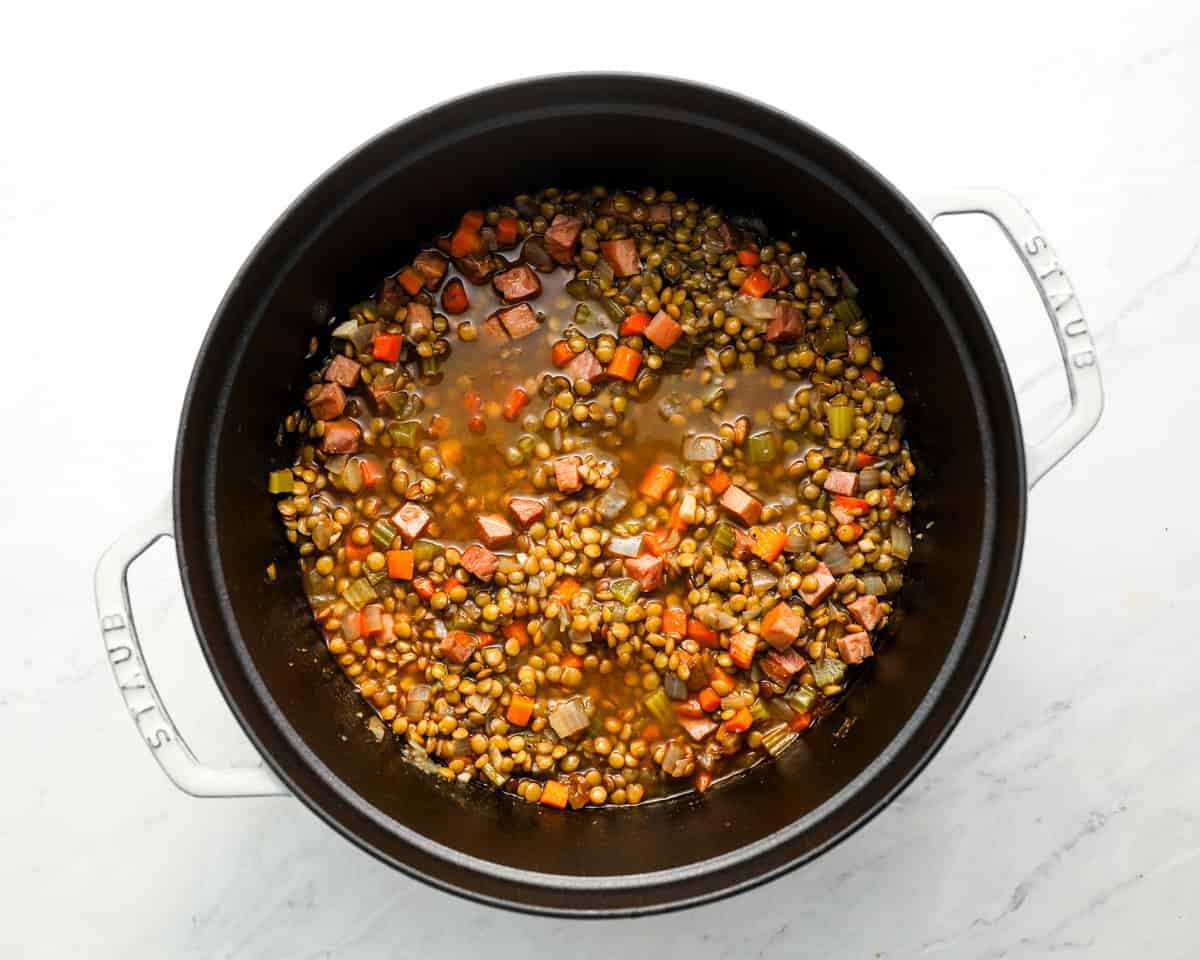 Simmering ham and lentil soup with visible chunks of ham, carrots, celery, and lentils in a rich broth.